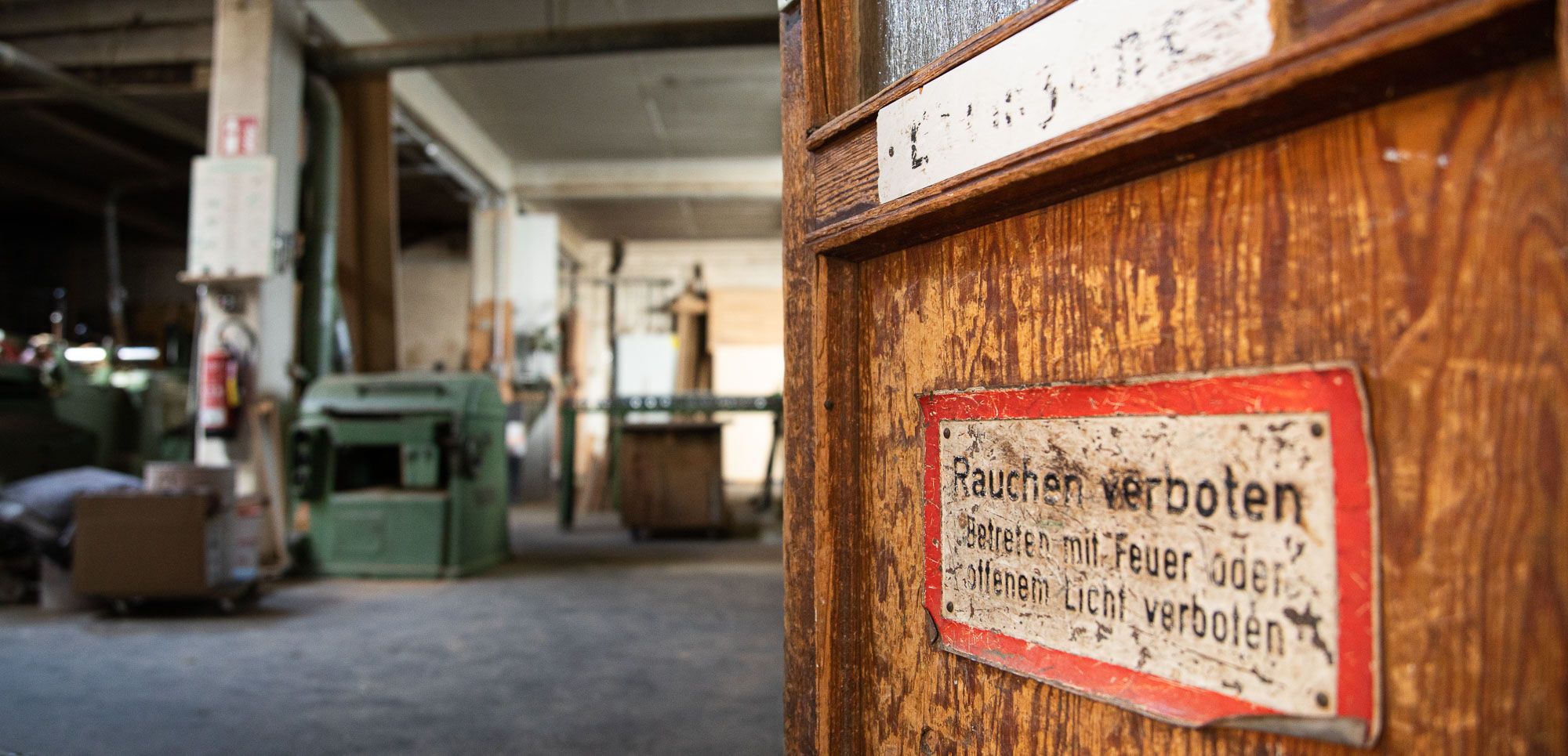 Die Aufnahme des Frankfurter Fotografen Fritz Philipp zeigt den Eingangsbereich einer alten Schreinerei, im Vordergrund ist die Holztür mit alten Schildern zu sehen, im Hintergrund die weitläufige Industriehalle, die zu einem Mietstudio wird, 2020: Great things to come