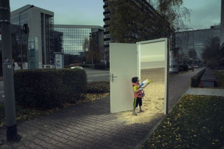 Das surrealistische Foto aus der Serie "Triologie der Türen" für die Darmstädter Tage der Fotografie zeigt einen kleinen Jungen mit Wasserpistole, der durch eine auf einer dunklen Straße stehende Zimmertür auf den sonnigen Sandstrand blickt, von dem Fotografen Fritz Phillipp aus Frankfurt im Rhein-Main-Gebiet
