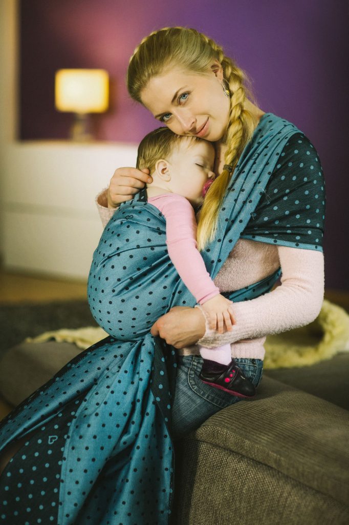 Portrait von einer auf dem Sofa sitzenden Mutter mit Baby in einem Tragetuch von Pollora, von dem Fotografen Fritz Phillipp aus Frankfurt im Rhein-Main-Gebiet