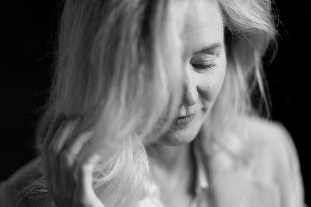 Schwarz-weiß Portrait einer Frau mit leicht geneigtem Kopf, die sanft eine Strähne ihres Haares berührt. Ihr Blick ist nach unten gerichtet, und ihr Ausdruck wirkt ruhig und nachdenklich. Fotografiert von dem Frankfurter Fotografen Fritz Philipp.