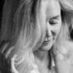 Schwarz-weiß Portrait einer Frau mit leicht geneigtem Kopf, die sanft eine Strähne ihres Haares berührt. Ihr Blick ist nach unten gerichtet, und ihr Ausdruck wirkt ruhig und nachdenklich. Fotografiert von dem Frankfurter Fotografen Fritz Philipp.