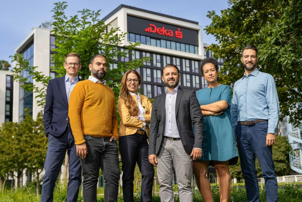 Eine diverse Gruppe von Mitarbeitern posiert selbstbewusst vor einem modernen Bürogebäude mit Deka-Logo. Fotografiert von dem Frankfurter Fotografen Fritz Philipp.
