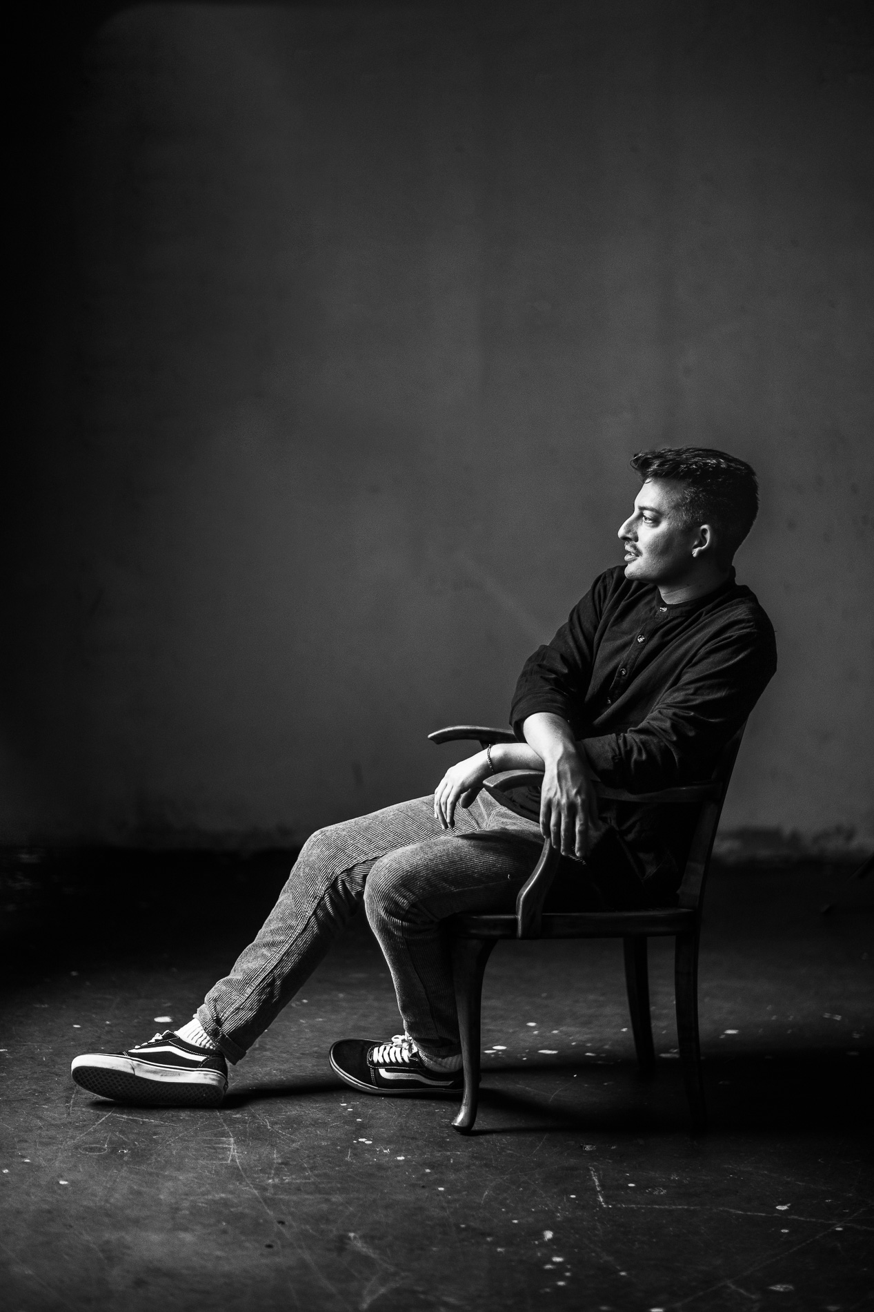 Joscha David Moret sitzt seitlich auf einem Stuhl im Fotostudio, die Arme auf den Armlehnen abgelegt