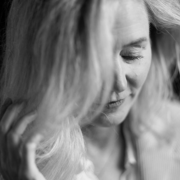 Schwarz-weiß Portrait einer Frau mit leicht geneigtem Kopf, die sanft eine Strähne ihres Haares berührt. Ihr Blick ist nach unten gerichtet, und ihr Ausdruck wirkt ruhig und nachdenklich. Fotografiert von dem Frankfurter Fotografen Fritz Philipp.