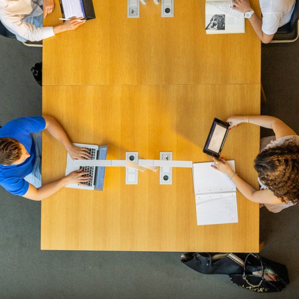 Vier Personen sitzen an einem großen Holztisch von oben fotografiert, arbeiten mit Laptops, Tablets und Notizbüchern. Fotografiert von dem Frankfurter Fotografen Fritz Philipp.