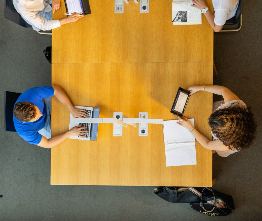 Vier Personen sitzen an einem großen Holztisch von oben fotografiert, arbeiten mit Laptops, Tablets und Notizbüchern. Fotografiert von dem Frankfurter Fotografen Fritz Philipp.