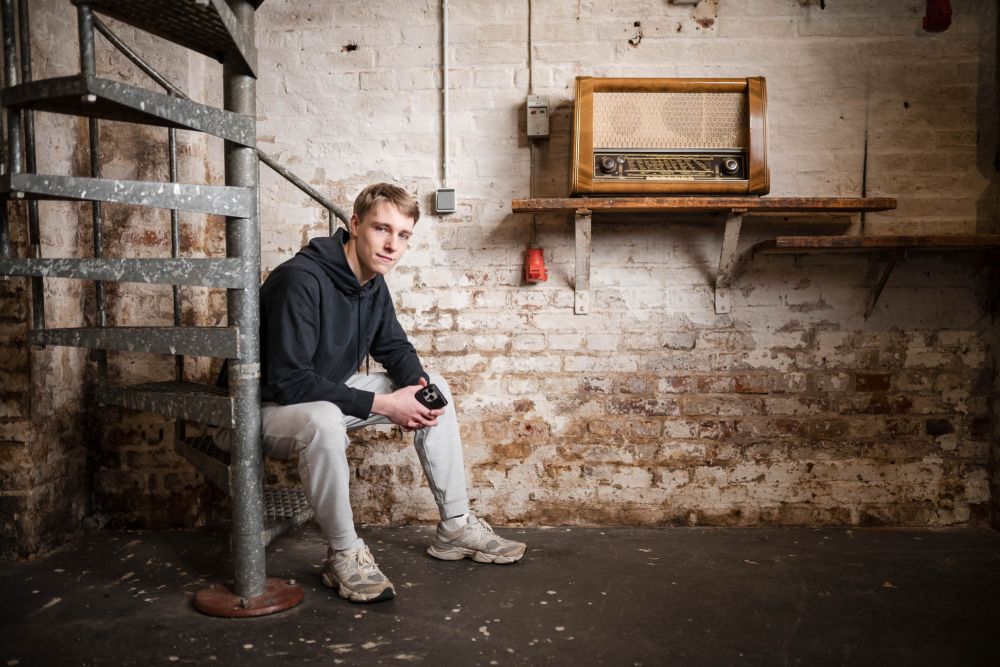 Jugendlicher im Hoodie sitzt an der Wendeltreppe, im Hintergrund ein altes Röhrenradio – Portrait beim Workshop Banking und Generation Alpha im Schärferaum