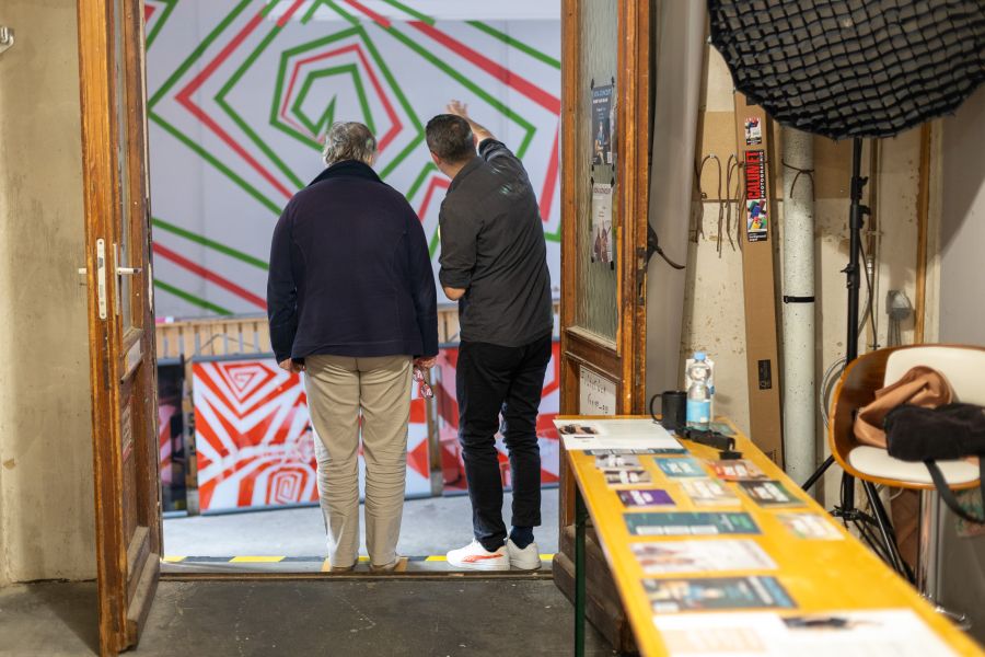 Zwei Besucher betrachten ein großformatiges Bild mit roten und grünen Linien hinter einer Holztür – KunstWerkStadt im Schärferaum Bad Homburg