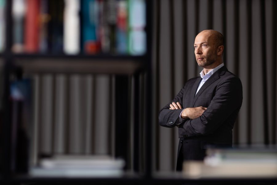 Ein Geschäftsmann steht hinter einem Bücherregal in einem dunklen Raum und schaut gedankenverloren in die Ferne. Fotografiert von dem Frankfurter Fotografen Fritz Philipp.