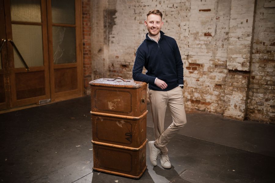 Junger Mann lehnt lässig an einer alten Holzkommode im Schärferaum – Portraitshooting Banking und Generation Alpha