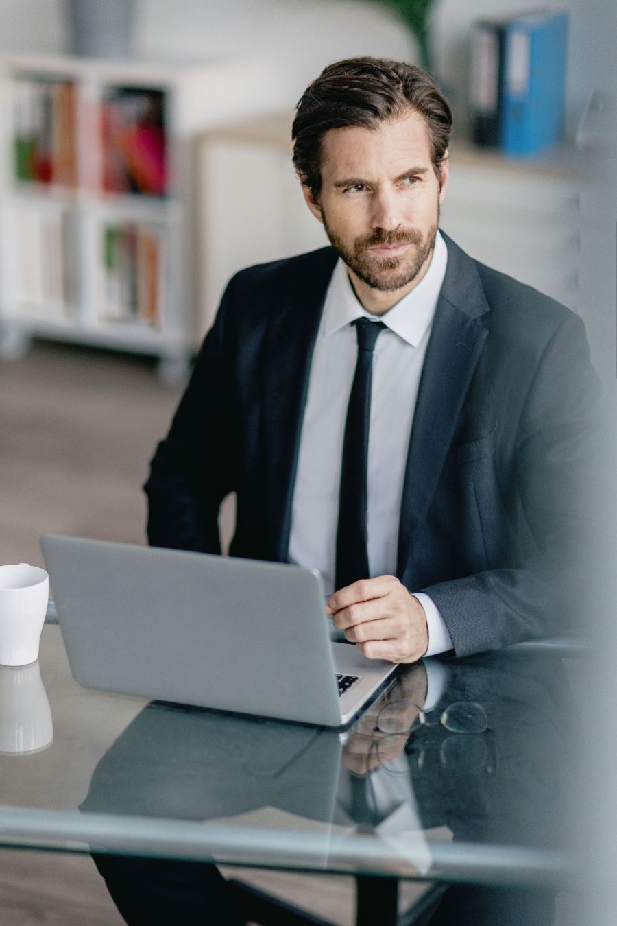 Ein Geschäftsmann sitzt in einem hellen Raum an einem Laptop und schaut gedankenversunken aus dem Fenster. Businessportrait im Schärferaum Bad Homburg.