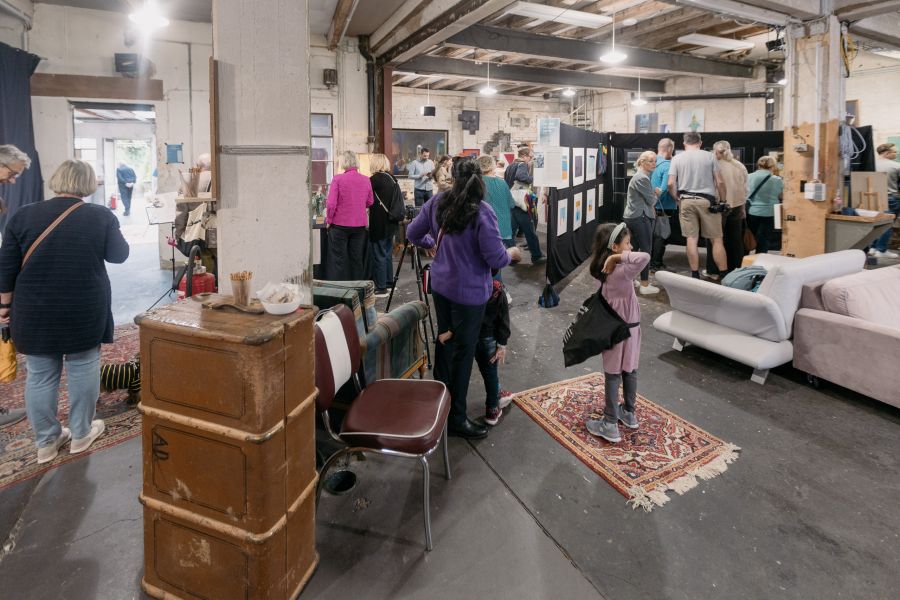 Blick in die gut besuchte Ausstellungshalle mit Sofas, Teppichen und Stellwänden – KunstWerkStadt im Schärferaum Bad Homburg