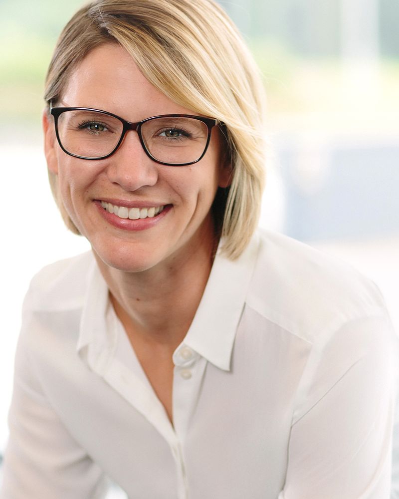 Nahaufnahme einer lächelnden Frau mit Brille und weißer Bluse vor hellem Hintergrund – Businessportrait von Fotograf Fritz Philipp, Bad Homburg
