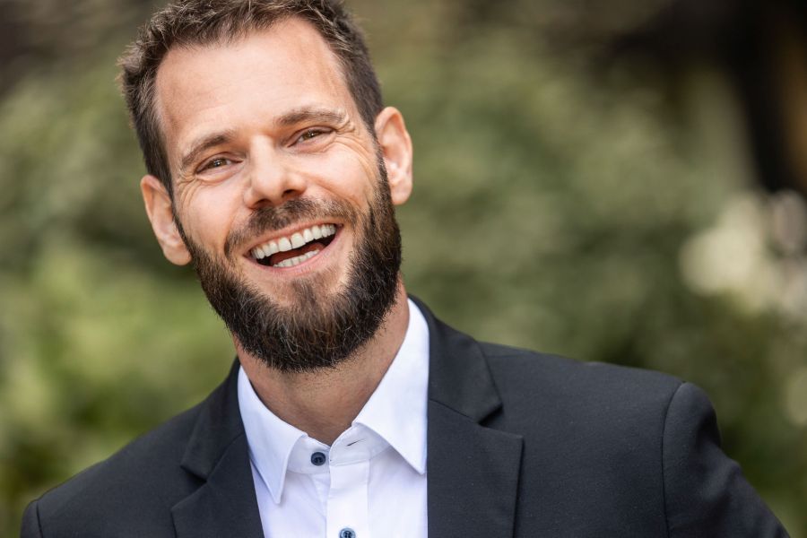 Ein Mann mit Bart in Business-Kleidung lacht herzlich in die Kamera, vor einem unscharfen grünen Hintergrund. Fotografiert von dem Frankfurter Fotografen Fritz Philipp.