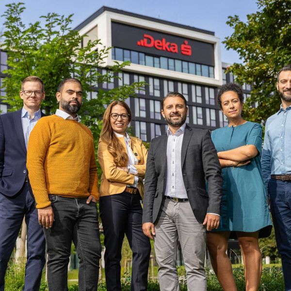 Eine diverse Gruppe von Mitarbeitern posiert selbstbewusst vor einem modernen Bürogebäude mit Deka-Logo. Fotografiert von dem Frankfurter Fotografen Fritz Philipp.