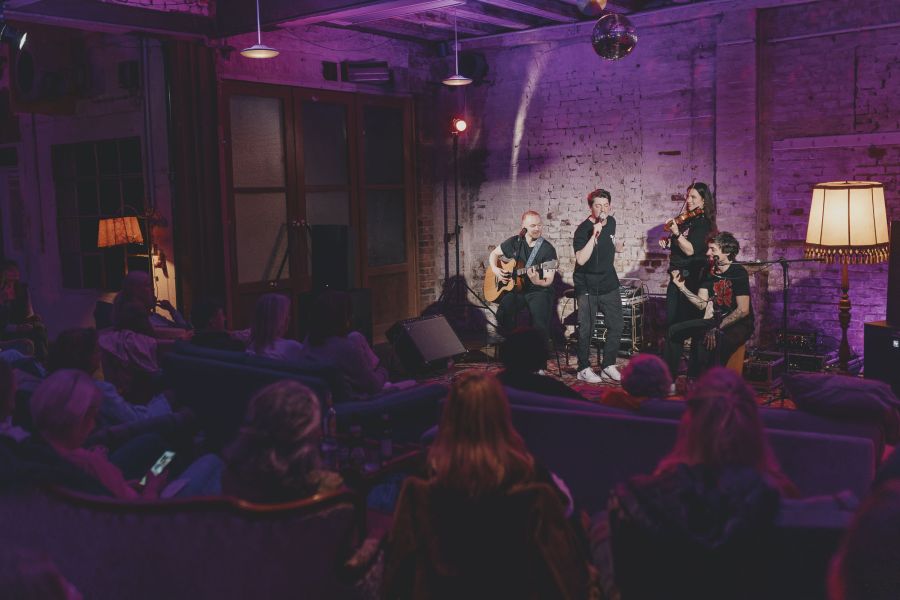 Sofakonzert im Schärferaum: Band vor Backsteinwand, Publikum auf Sofas, Stehlampe und Discokugel – Sofakonzert von Die Dinners im Schärferaum