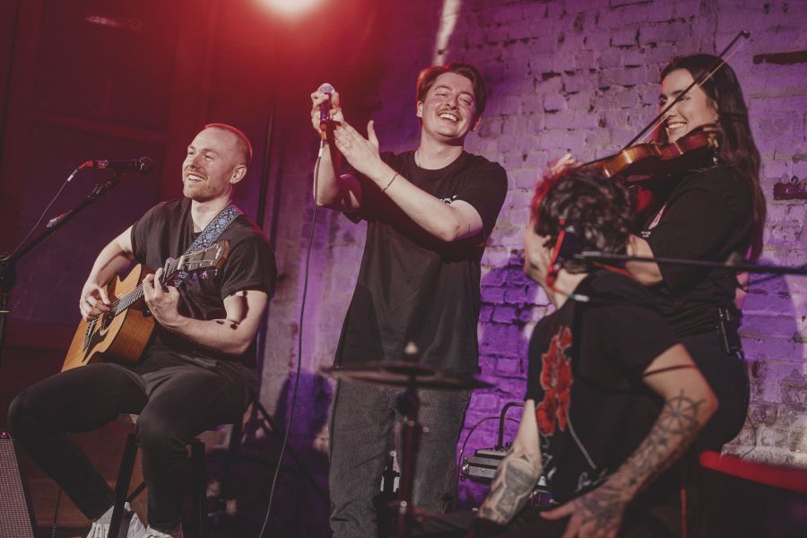 Band lacht und klatscht, Geigerin spielt mit einem Lächeln – Sofakonzert von Die Dinners im Schärferaum