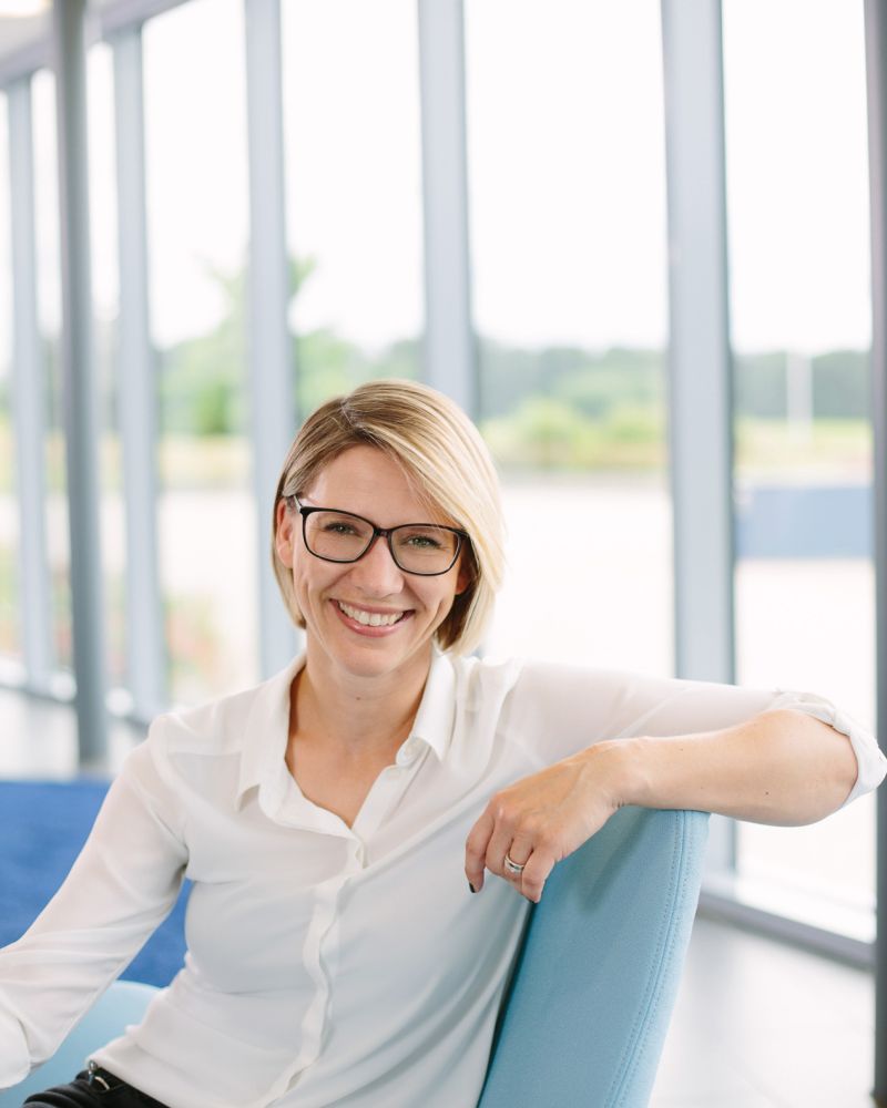 Frau mit Brille und weißer Bluse sitzt entspannt in einem blauen Sessel vor großen Fenstern – Businessportrait von Fotograf Fritz Philipp, Bad Homburg