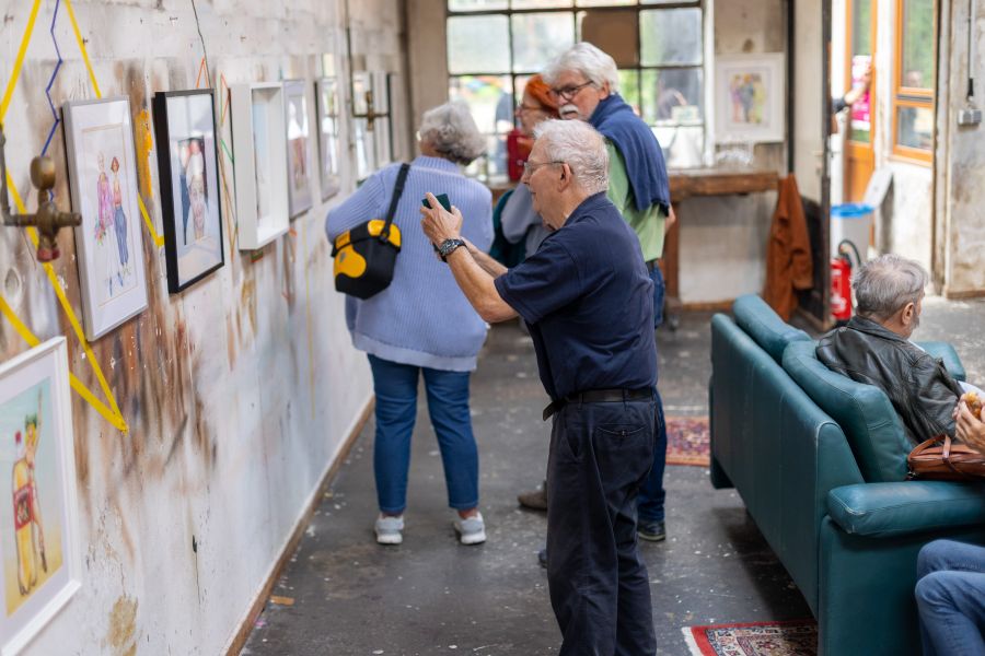 Ältere Besucher betrachten gerahmte Zeichnungen an einer Backsteinwand, rechts ein grünes Sofa – KunstWerkStadt im Schärferaum Bad Homburg